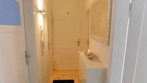 A narrow hallway with a wooden floor, a black mat, a white door, a white wall with a mirror, and a white cabinet with a bowl on top. - Private apartment Angelika NEW (Lorch)
