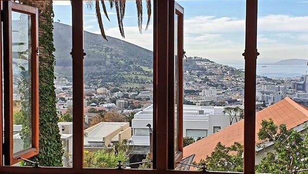 A view through a window with wooden frames, overlooking a cityscape with buildings, a hill, and a body of water. - Redbourne Hilldrop B&B (Cape Town)