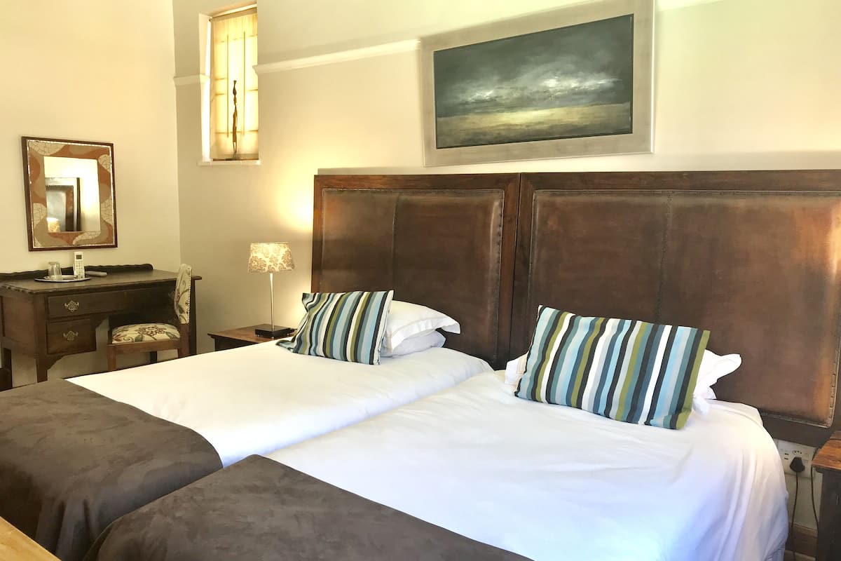 A hotel room with a large bed, a desk with a lamp, a mirror, and a painting on the wall.