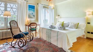 Ein Schlafzimmer mit einem Bett, einem Schaukelstuhl, einem Schreibtisch und einem Fenster mit Vorhängen.