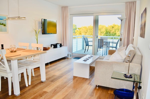 A modern living room with a dining area, a sofa, a coffee table, and a TV mounted on the wall.
