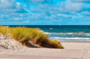 A beach with sand, grass, and the ocean under a partly cloudy sky.