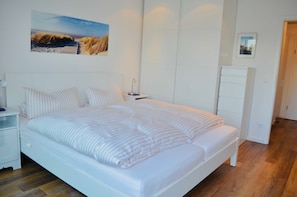 A bedroom with a large bed, a nightstand, a dresser, and a wall-mounted picture.