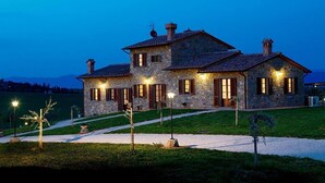Una casa de piedra con varias chimeneas, un camino de grava y una entrada bien iluminada.