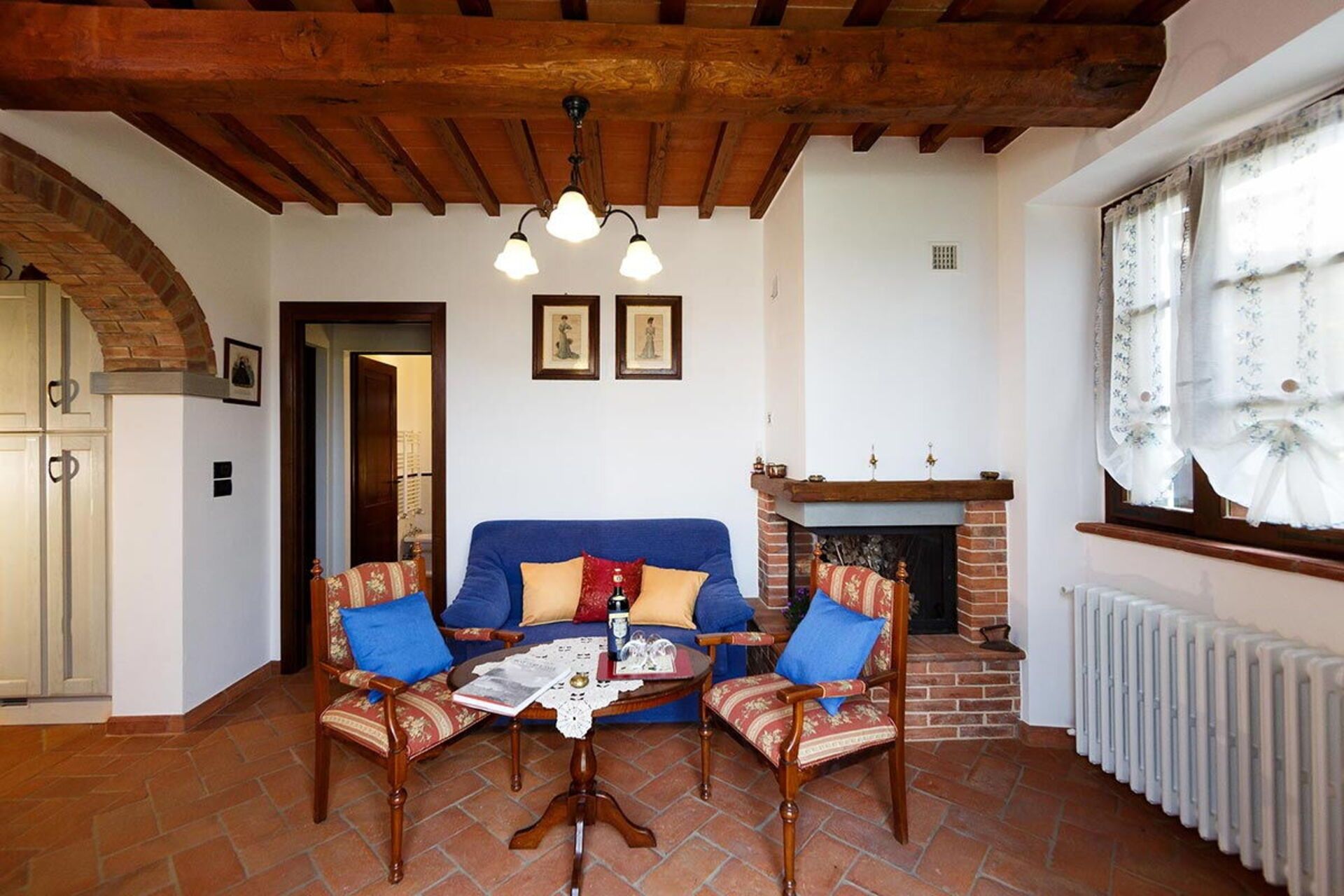 A living room with a fireplace, a blue sofa, two armchairs, and a tiled floor.