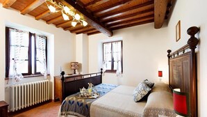 Un dormitorio acogedor con techo de madera, una cama con colcha estampada, una mesita de noche con lámpara y una ventana con cortinas.
