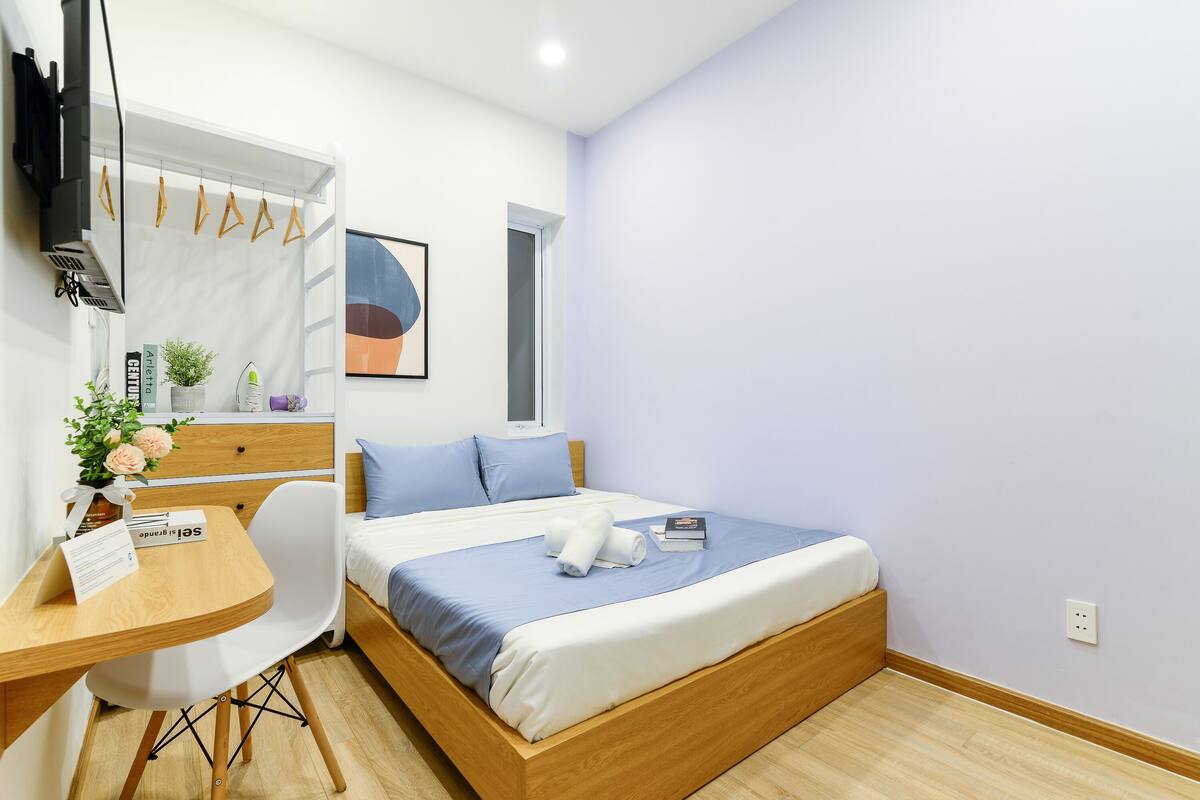 Un dormitorio con una cama, un escritorio, una silla, una mesita, una planta y una ventana.