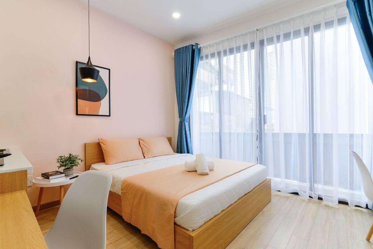 Una habitación de hotel moderna con cama, mesita de noche, silla y un gran ventanal con cortinas.