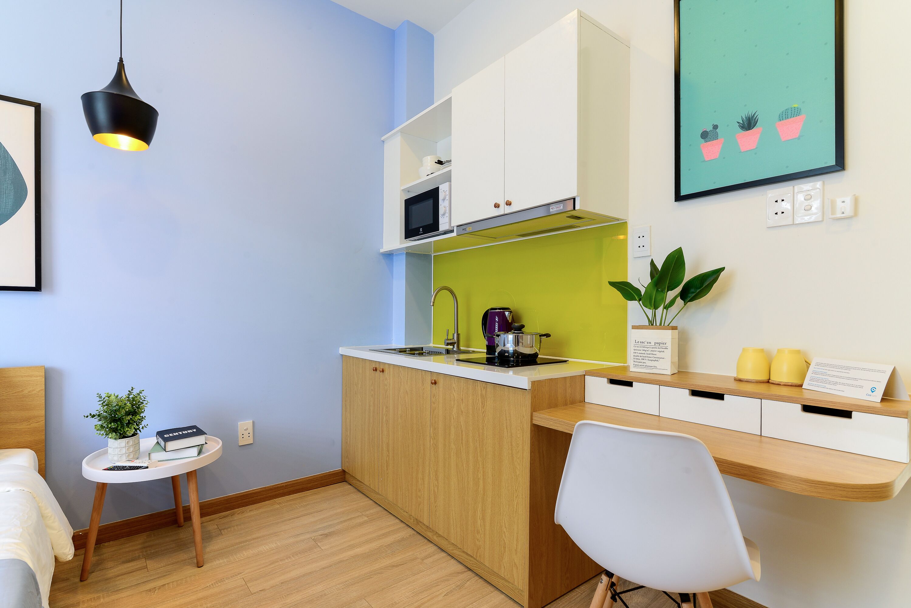 Een compacte keuken met een magnetron, waterkoker en een klein eethoekje met een stoel en een tafel.