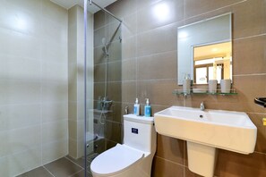 Un baño moderno con ducha envuelta en vidrio, un inodoro y un lavamanos con espejo superior.