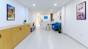 En modern hotellobby med en receptionsdisk, en blå soffa, en grå fåtölj och träskåp.