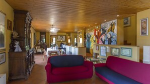 A cozy living room with a wooden ceiling, a red and blue sofa, a dining area with a table and chairs, and a kitchen in the background. - Villa / Independent home in Lucca with 4 bedrooms sleeps 8 (Lucca)