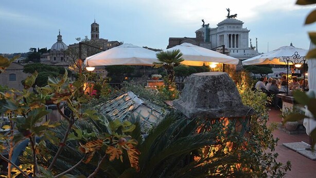 An outdoor seating area with umbrellas, stone structures, and a view of historical buildings. - Residenza Maritti Classic Rooms (Rome)