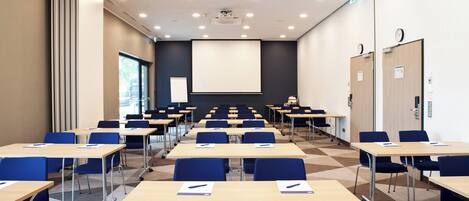 A conference room with multiple tables and chairs, a projector screen, and a clock on the wall.