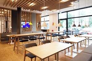 A modern restaurant with wooden tables and chairs, a digital menu display, and large windows offering a view of the outside. - Holiday Inn Express Darmstadt by IHG (Darmstadt)