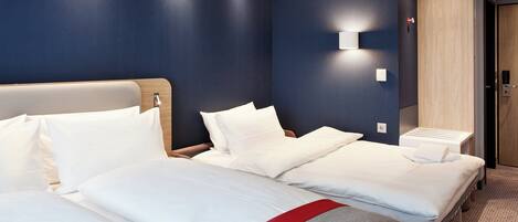 A hotel room with two beds, a wooden headboard, a bedside table, and a wall-mounted light.