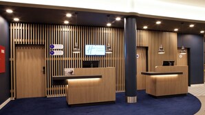 A reception area with a wooden reception desk, a digital display, and a blue carpet. - Holiday Inn Express Darmstadt by IHG (Darmstadt)