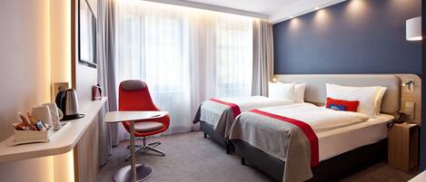 Una habitación de hotel con dos camas, un escritorio, una silla y un ventanal con cortinas.