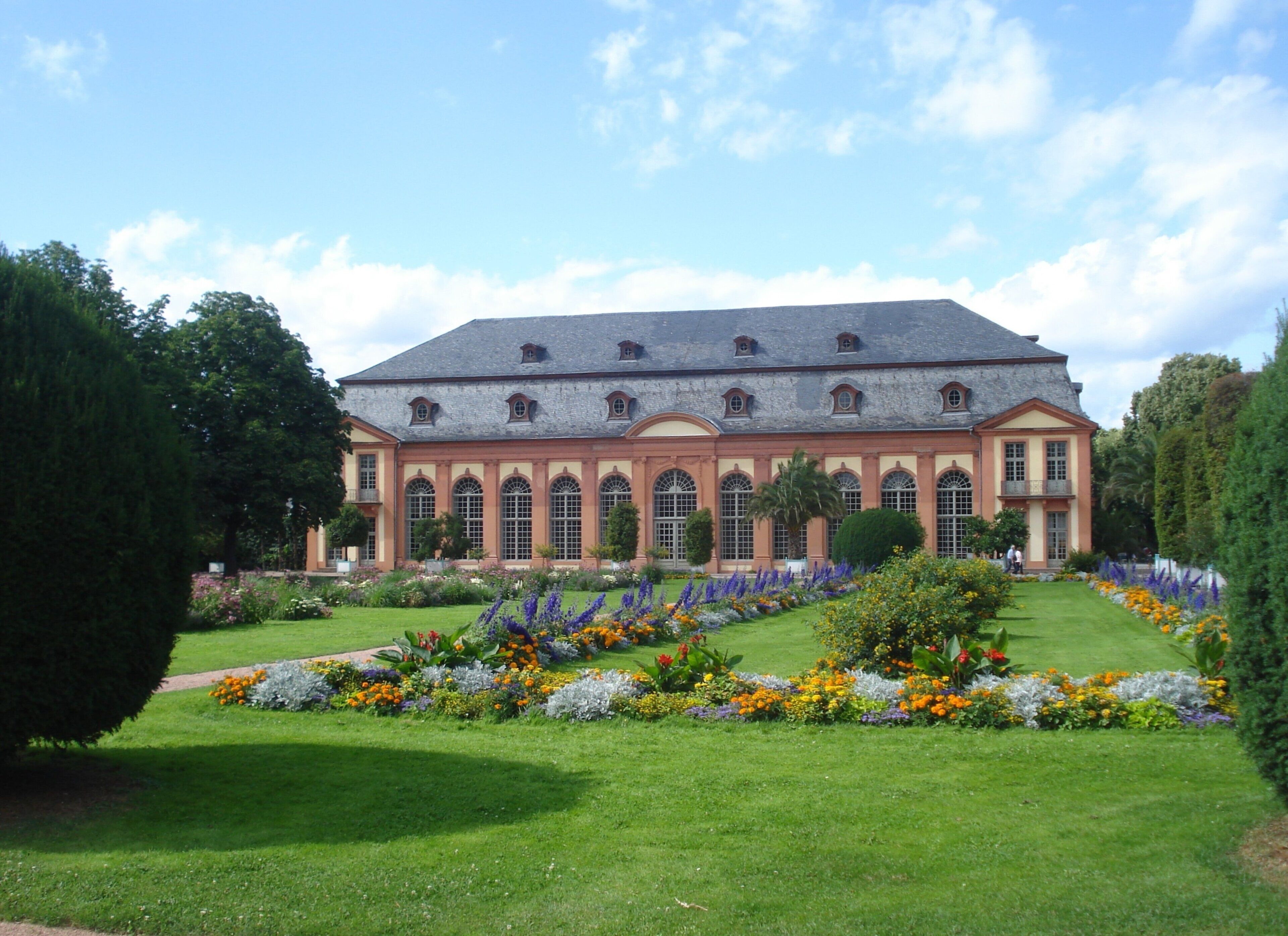 A large building with a symmetrical facade, multiple windows, and a well-maintained garden with various flowers and shrubs.