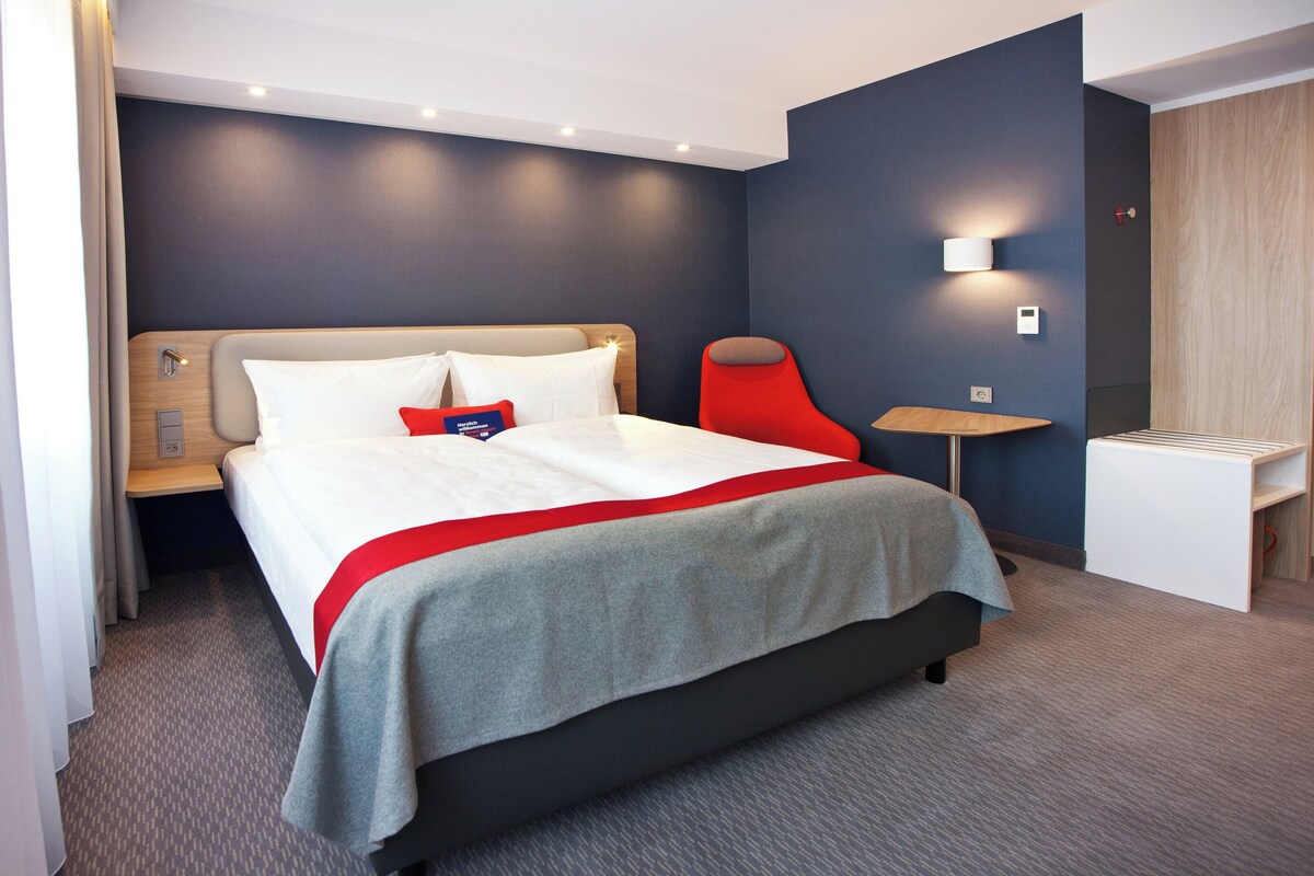 A hotel room with a bed, bedside table, and a small desk.
