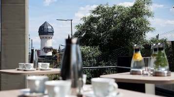 A terrace with tables set for tea, a lighthouse in the background, and a chain-link fence.