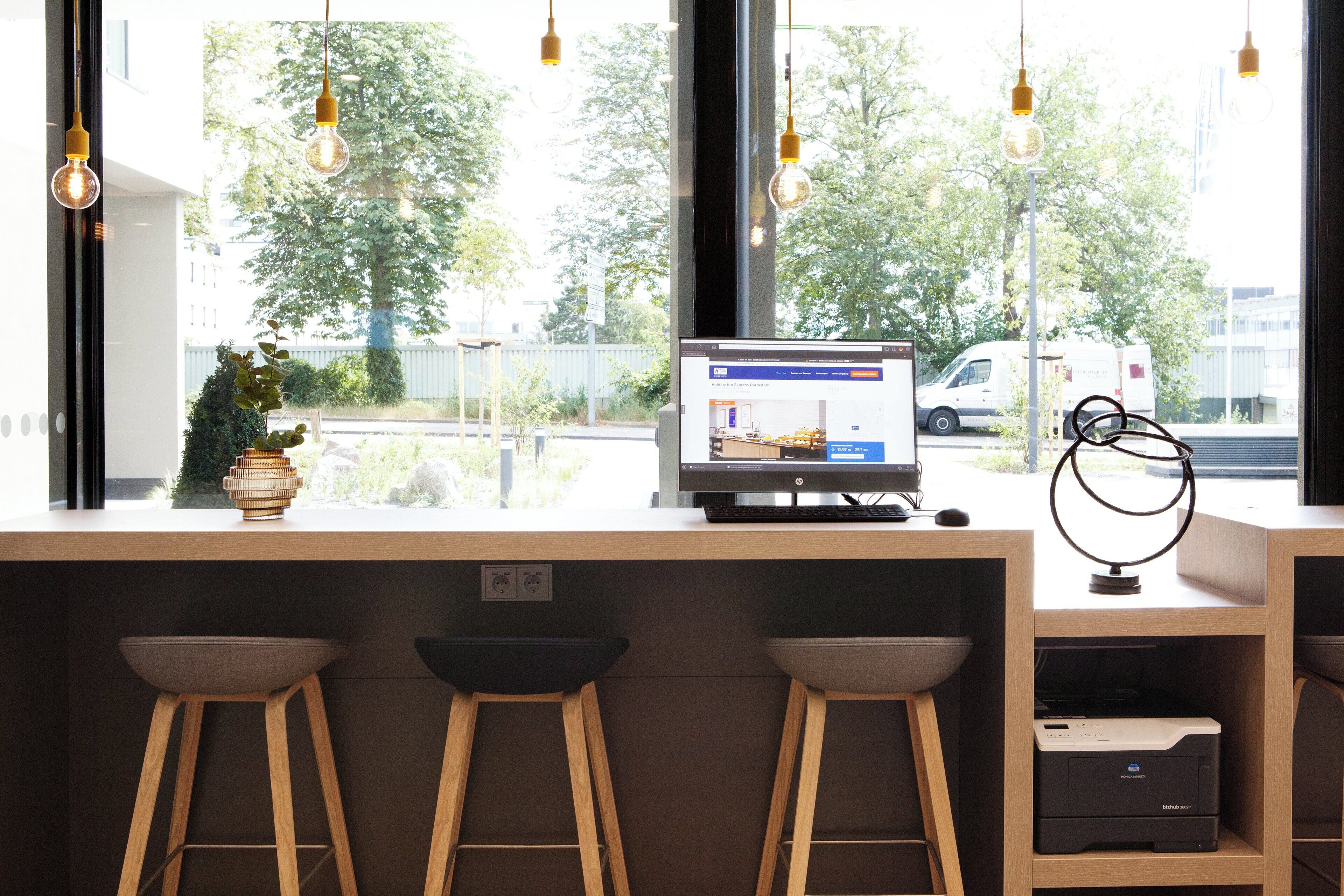 Zona de bar moderna con un monitor de computadora mostrando un sitio web, taburetes de madera y vistas a la calle.
