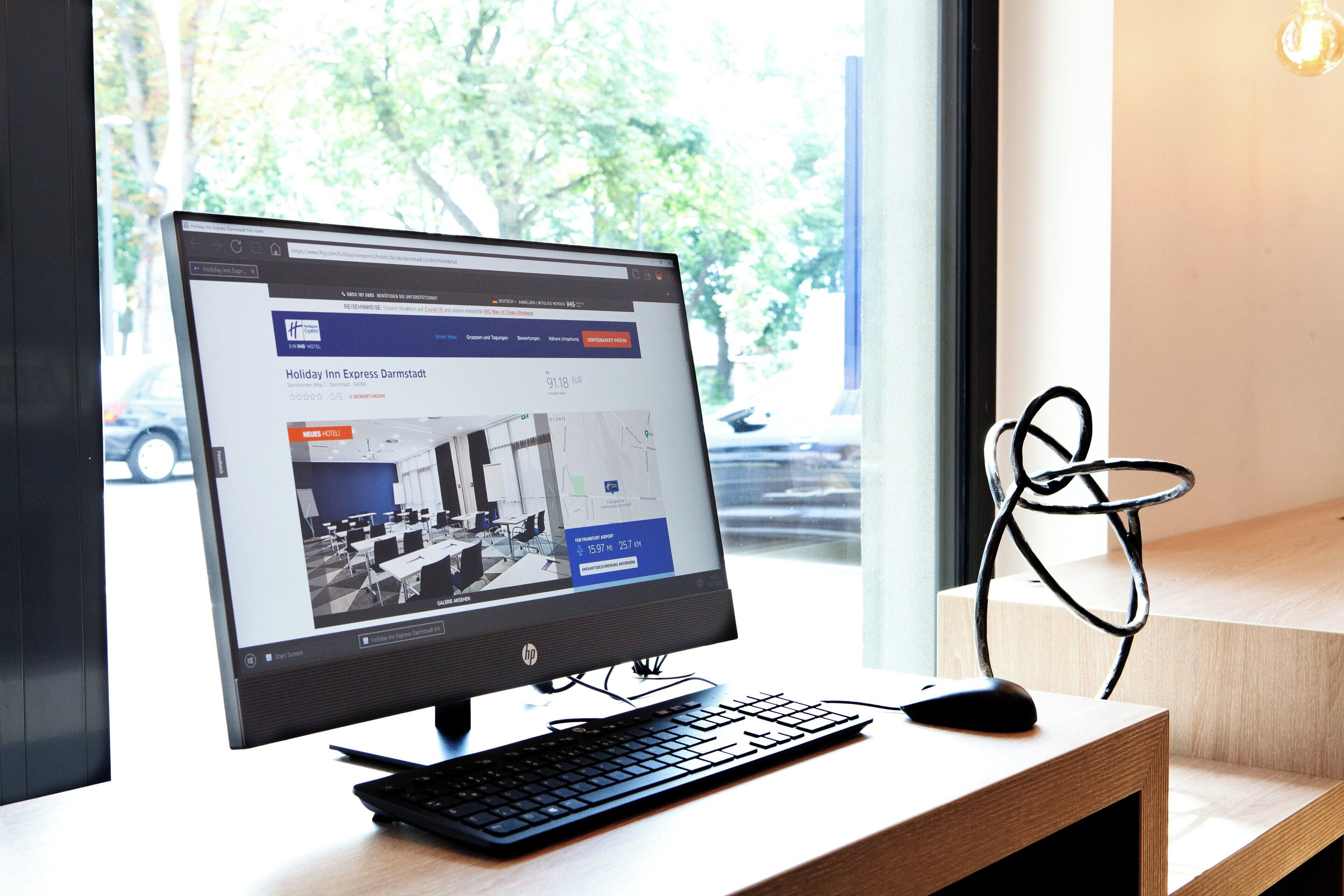Una computadora de escritorio con un sitio web de reservas de hotel abierto, un teclado y un ratón sobre un escritorio de madera.