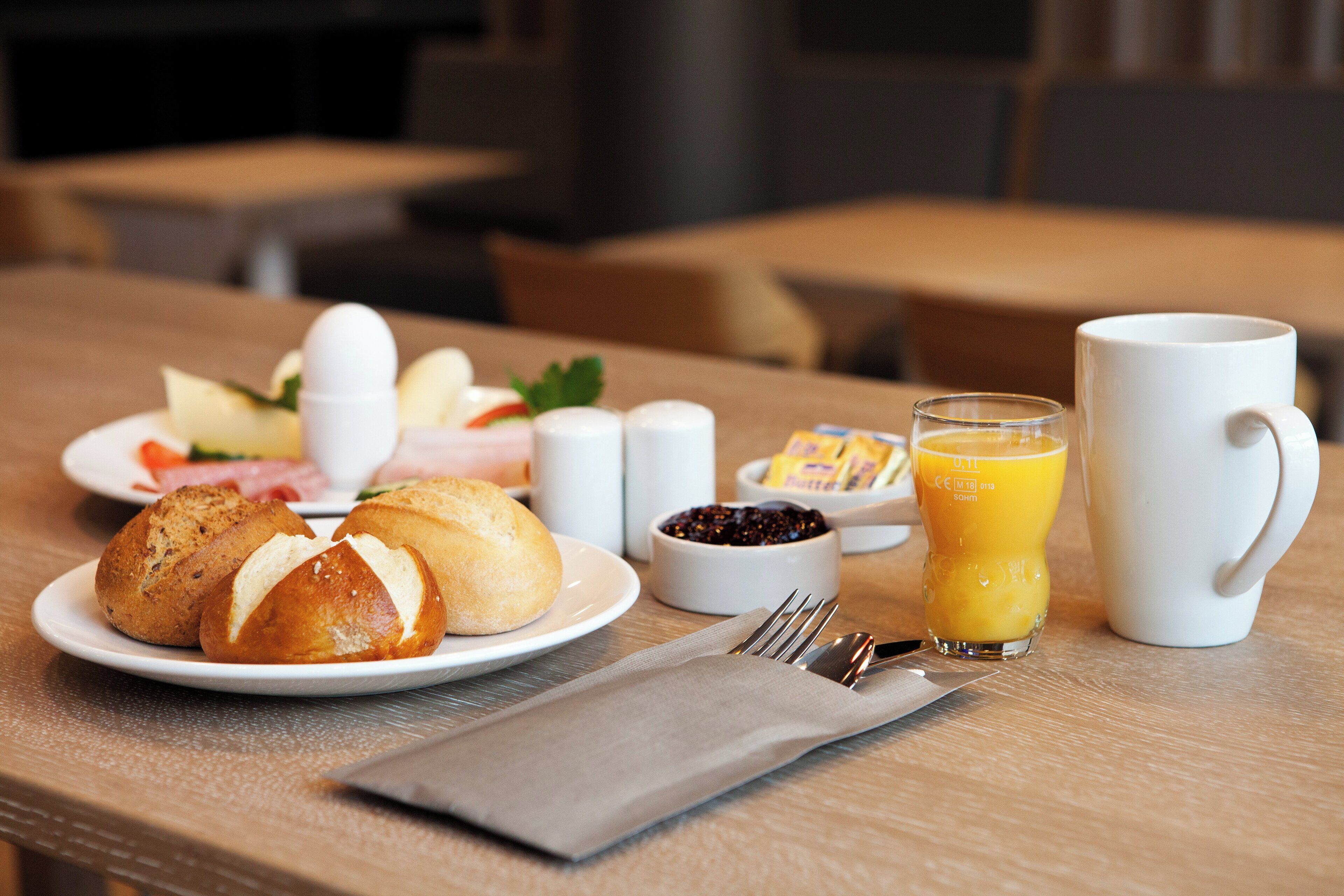 A breakfast setting with bread, eggs, butter, jam, and a glass of orange juice on a table.