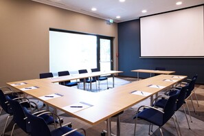 A conference room with a large table, chairs, a projector screen, and a door leading outside. - Holiday Inn Express Darmstadt by IHG (Darmstadt)