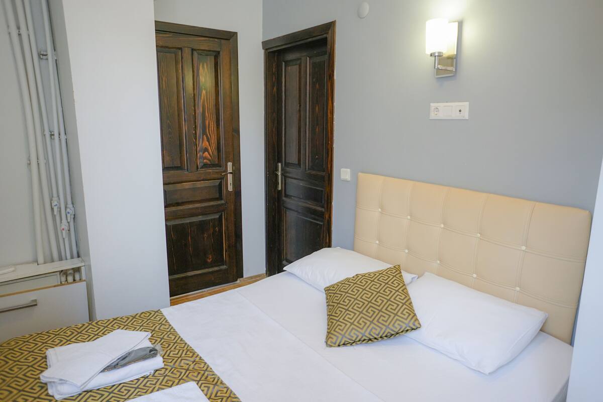 A hotel room with a bed, two doors, a light fixture, and a towel rack.