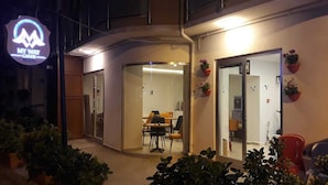A hotel entrance with a glass door, a dining area with tables and chairs, and potted plants. - My Way Cadde Butik Otel (Adalar)
