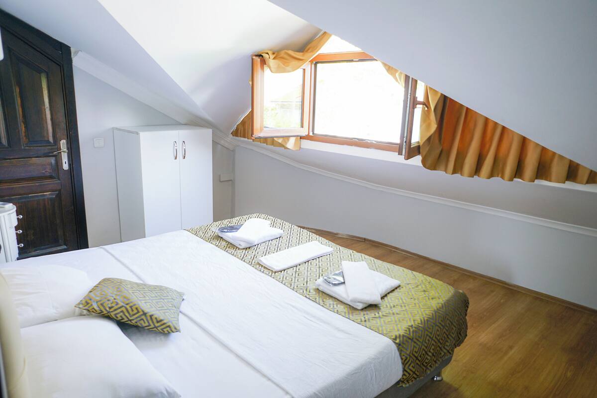A hotel room with a bed, a wardrobe, a window with curtains, and a skylight.
