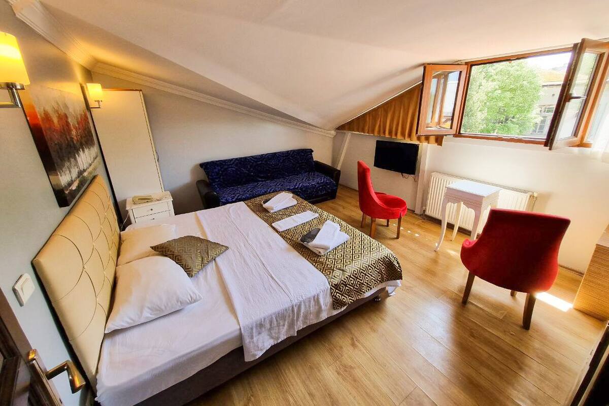 A bedroom with a bed, a red chair, a desk, and a window.