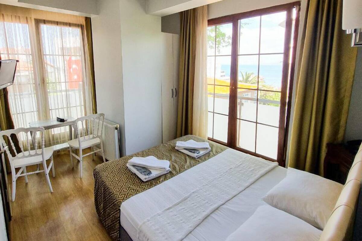 A hotel room with a bed, a small table with chairs, a window with curtains, and a view of the outside.
