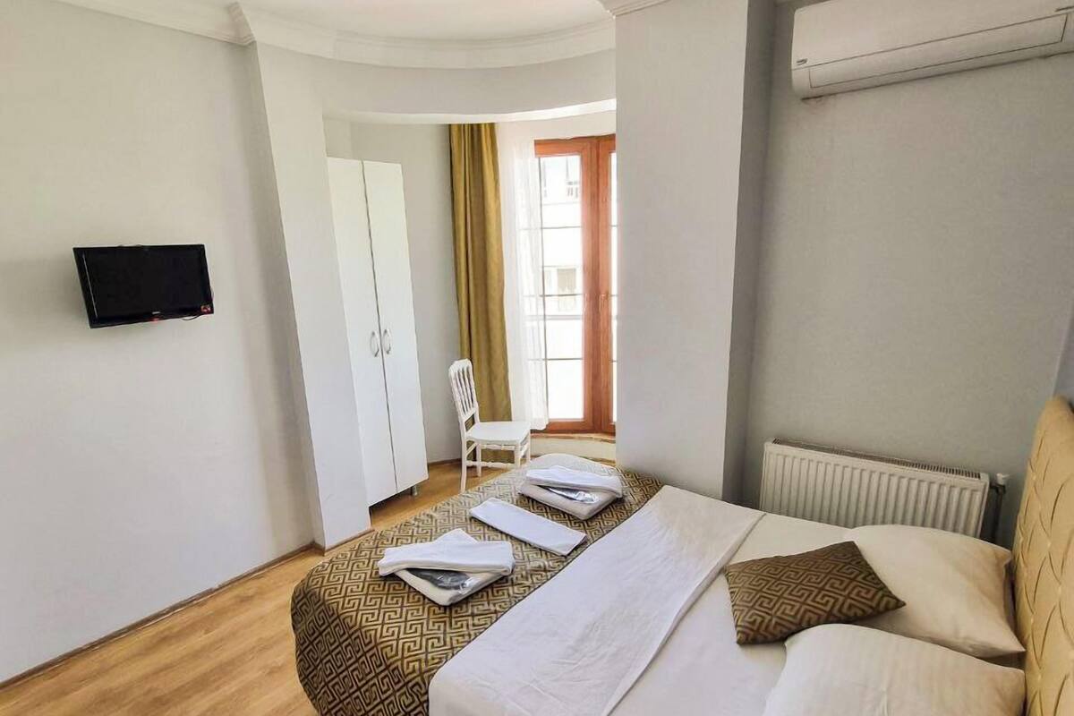 A hotel room with a bed, a chair, a TV, and a window with curtains.