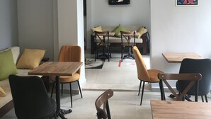 A modern dining area with wooden tables and chairs, a sofa, and a TV mounted on the wall. - My Way Cadde Butik Otel (Adalar)