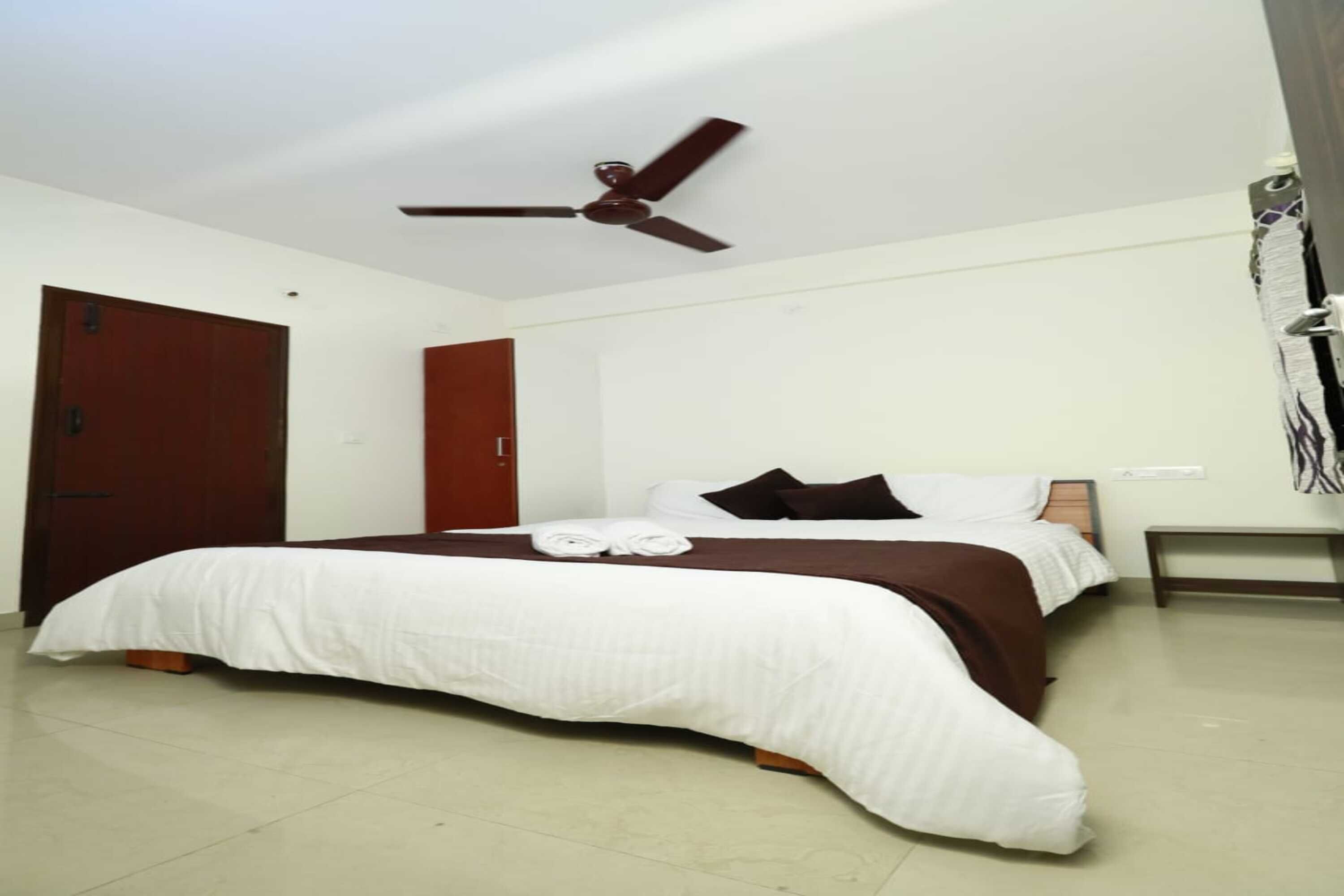 A hotel room with a bed, a ceiling fan, a wooden door, and a bench.