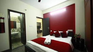 A modern hotel room with a large bed, red and white bedding, a bedside table with a plant, and a red accent wall.