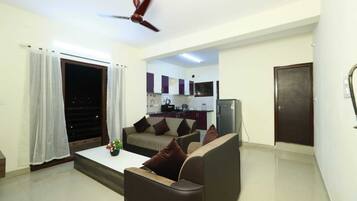 A living room with a sofa, a coffee table, and a ceiling fan. There is a kitchen visible through an open doorway.