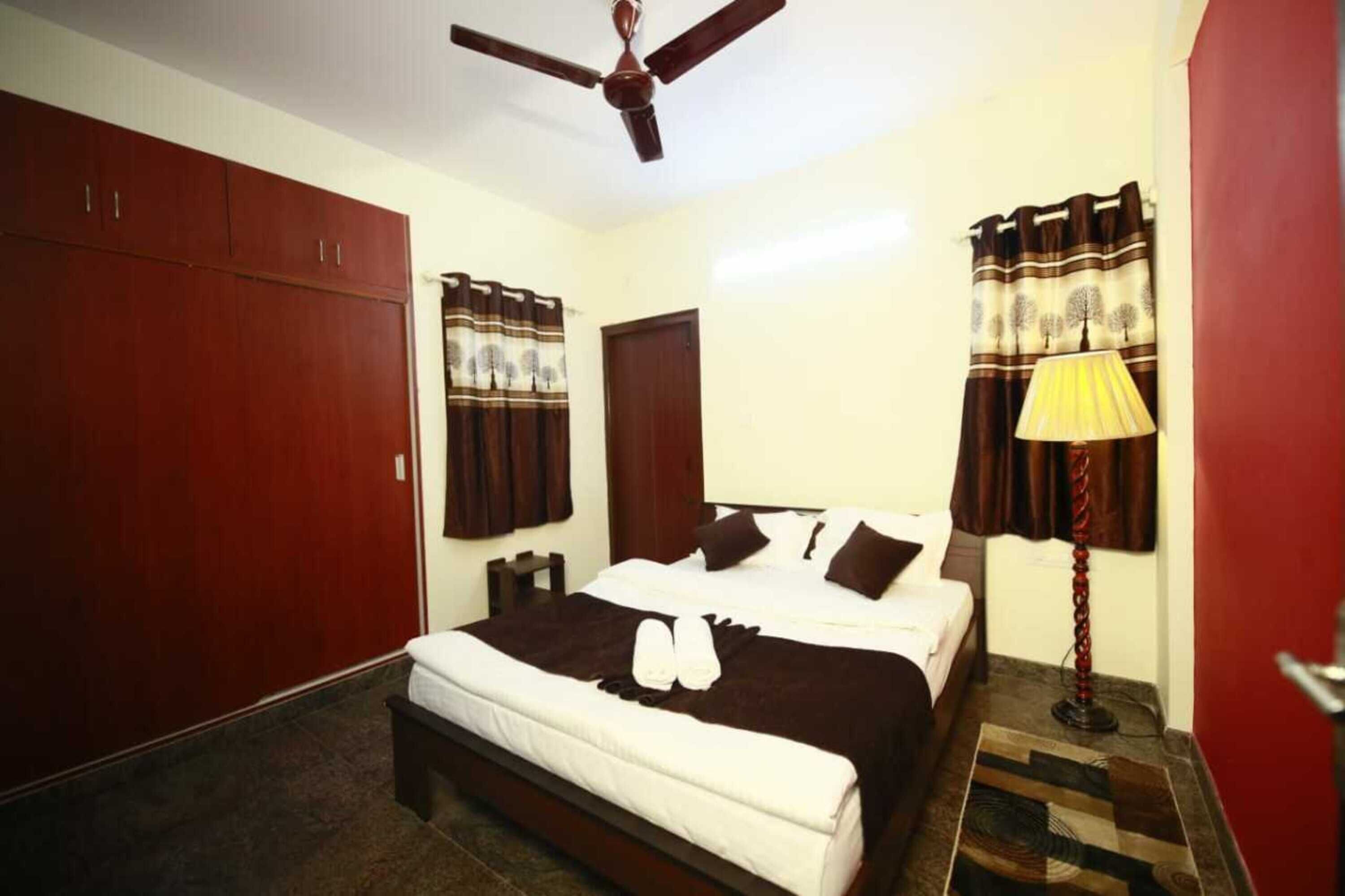 Een hotelkamer met een bed, een plafondventilator, een kledingkast, een nachtkastje en gordijnen.