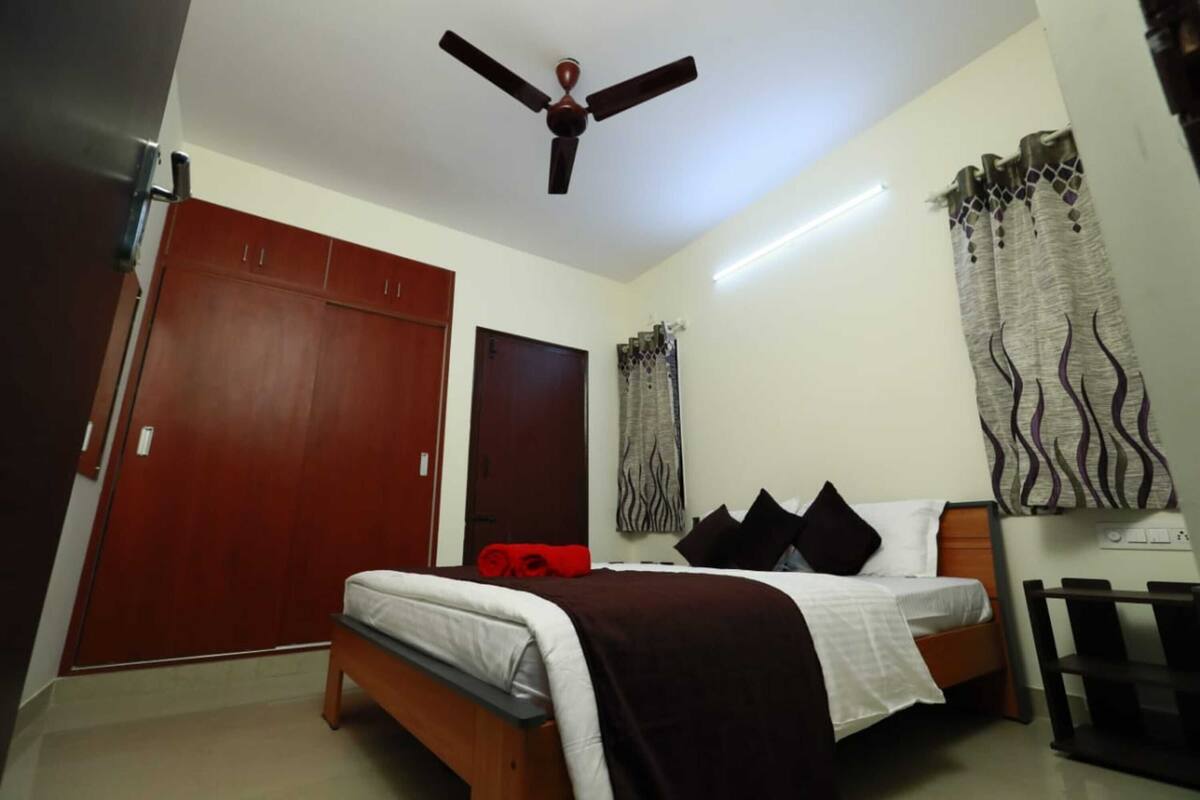 Un dormitorio con cama, ventilador de techo, armario y cortinas.
