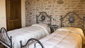 Une chambre avec deux lits, un mur en pierre et une porte en bois.