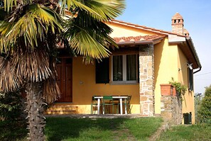 A yellow building with a stone facade, a wooden door, and a small balcony with a table and chairs.