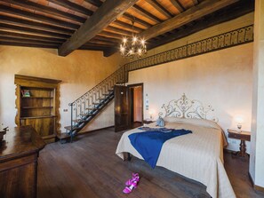 A bedroom with a wooden floor, a bed with a blue blanket, a staircase with a wrought iron railing, and a chandelier. - Villa / Independent home in Ponte A Moriano with 6 bedrooms sleeps 14 (Lucca)