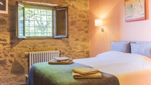 A room with a stone wall, a window with a view of trees, a radiator, a bed with a green blanket, and a painting on the wall. - Villa / Independent home in Ponte A Moriano with 6 bedrooms sleeps 14 (Lucca)