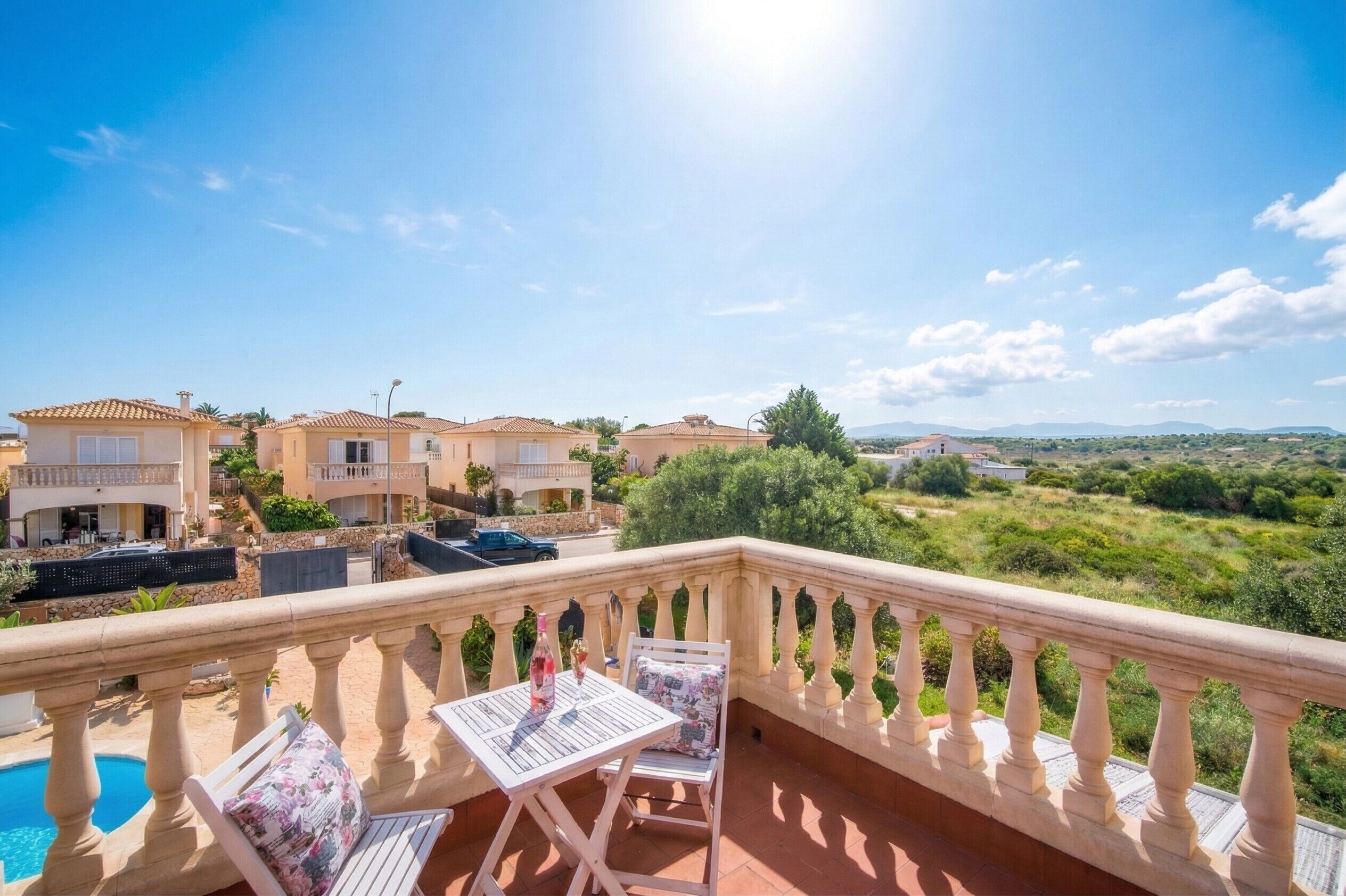 Een balkon met een zwembad, buitenmeubilair en uitzicht op villa's en groen.