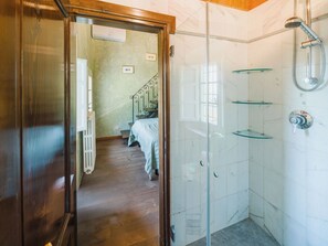 Une chambre d’hôtel avec une porte en bois, un lit recouvert d’une courtepointe à rayures, un radiateur, un escalier et une cabine de douche en verre.