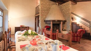 Un coin repas agrémenté d’une cheminée en pierre, de chaises en bois et d’une longue table dressée pour le repas.