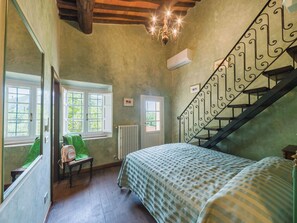 Une chambre à coucher comprenant un lit, une chaise, une fenêtre, un radiateur et un escalier avec une rampe en fer forgé.