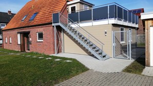Ein zweigeschossiges Gebäude mit rotem Ziegeldach, einem Glasbalkon und einer Treppe, die zum oberen Stockwerk führt.